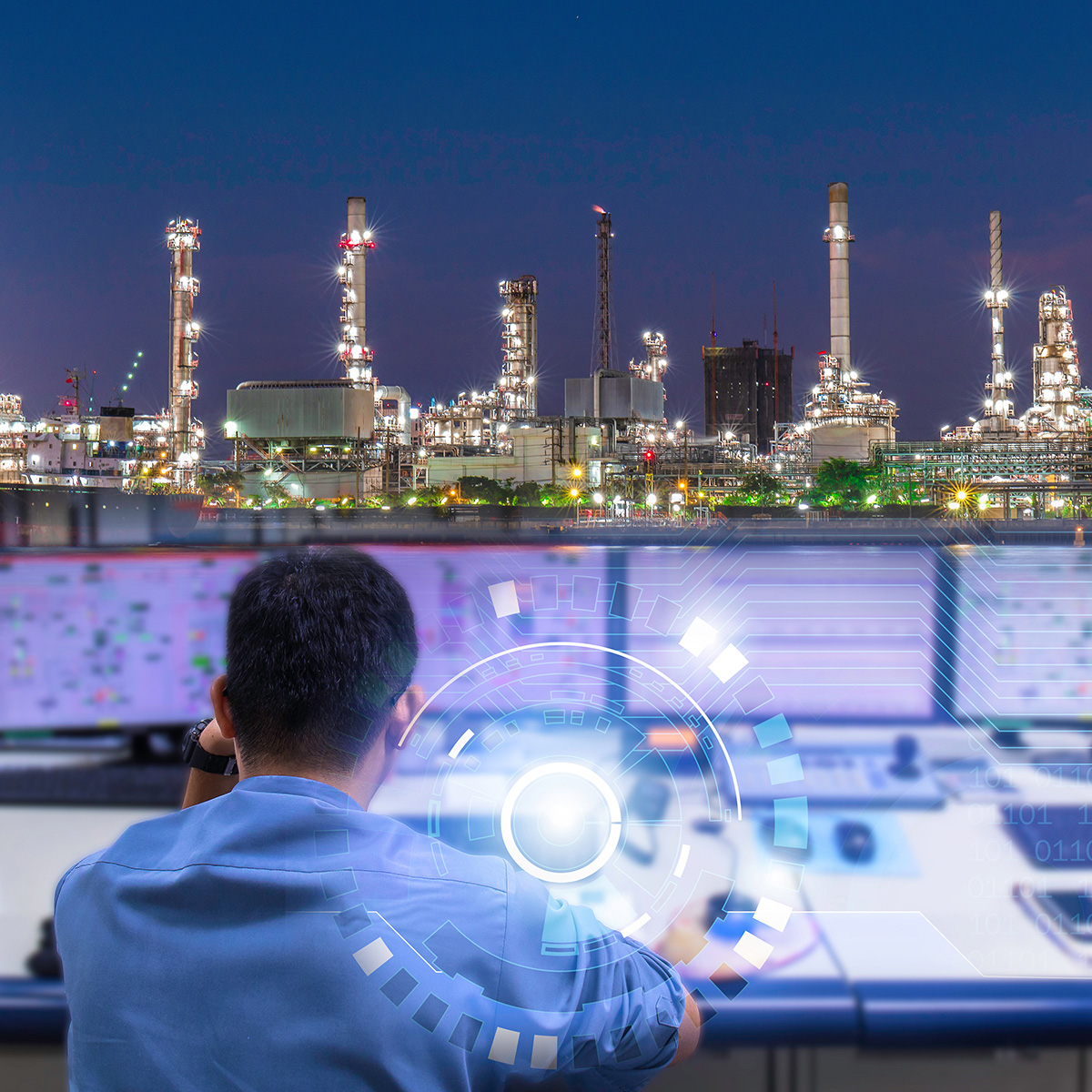 Person viewed from the back in a control room. Petroleum production plant in background.