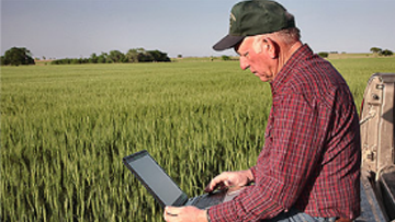 Un propriétaire foncier assis près d’une terre cultivée consulte un ordinateur portatif.