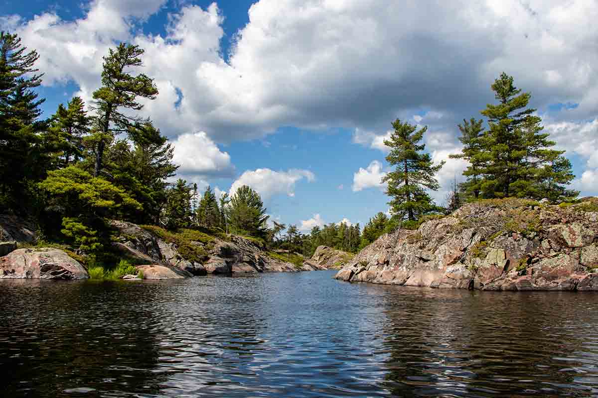 Roches, arbres, ciel bleu, nuages blancs et eau en été sur la rivière